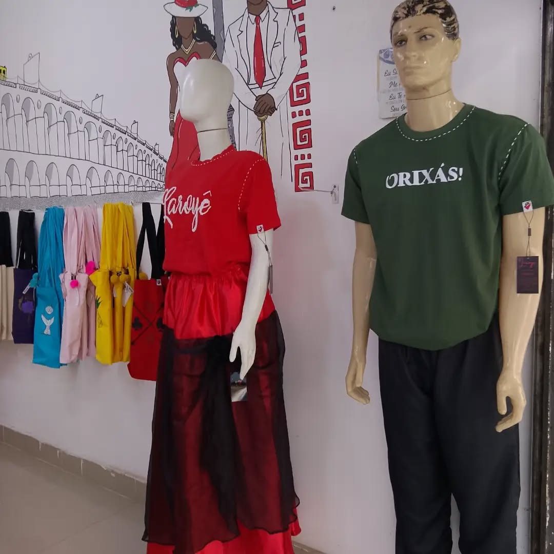 Vitrine com manequins em roupas do axé e fileira de ecobags coloridas com símbolos da tradição